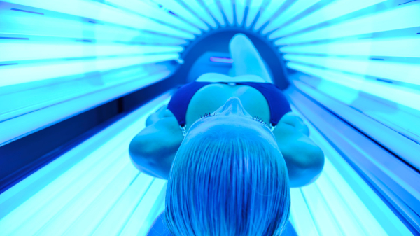 A woman lays in a tanning bed surrounded by blue lights.